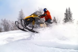 Snowmobiler jumping a drift.