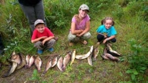 Young kids sitting on grass with fish they caught